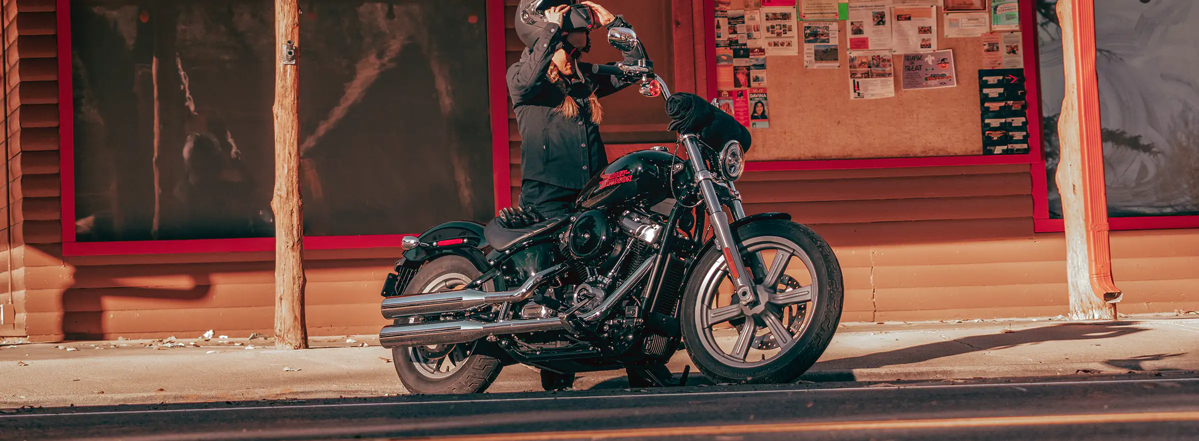 Rider standing next to a 2024 Harley-Davidson Softail Standard while putting on helmet.